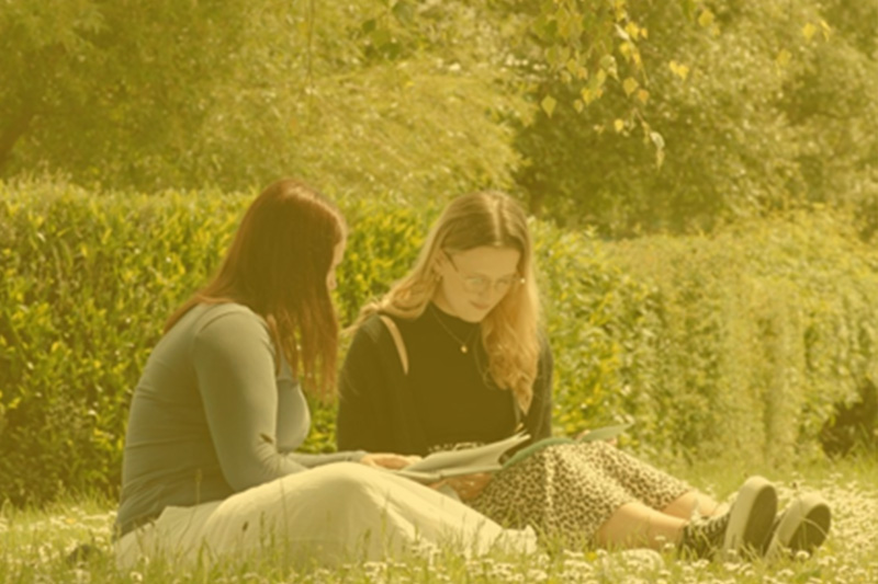 Two students sitting on the grass in the sunshine